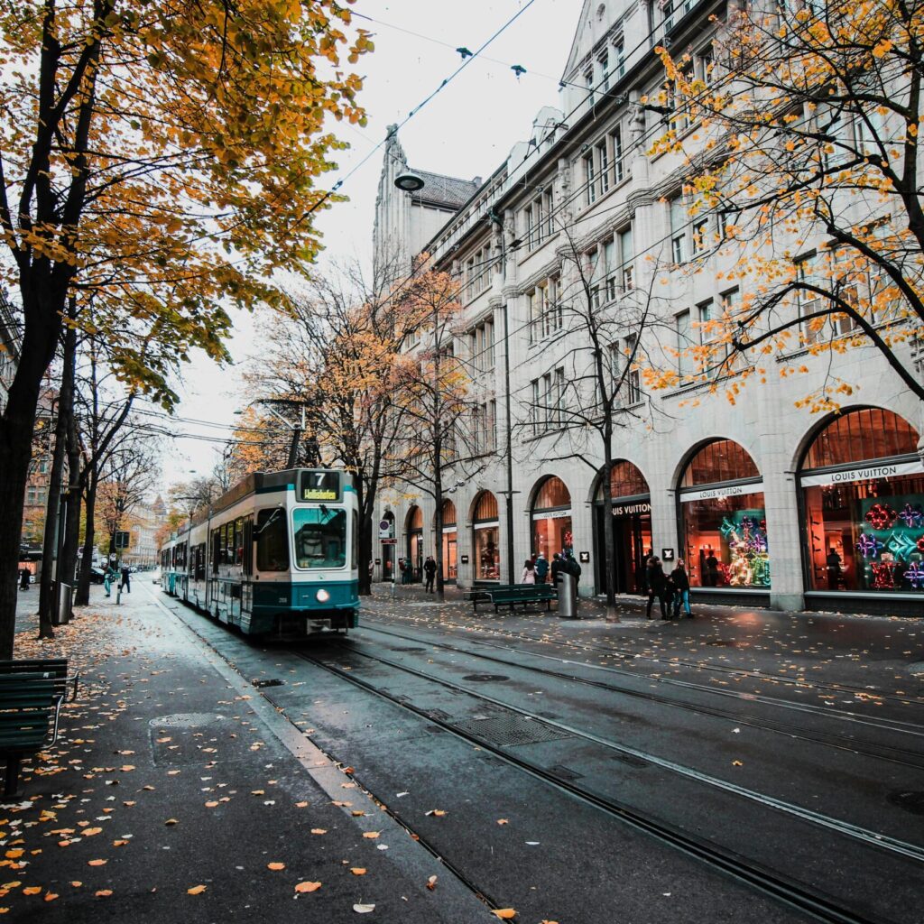 A tram travels down a leaf-strewn street in autumnal Zürich, Switzerland's urban landscape.
